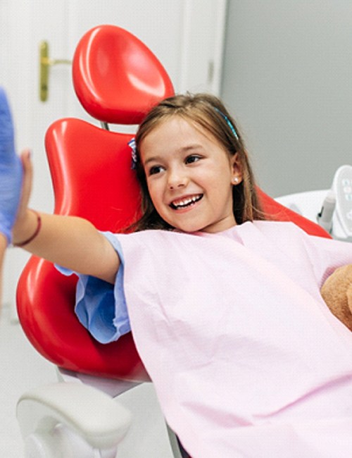 A little girl holding a teddy bear and giving her dental hygienist a high-five